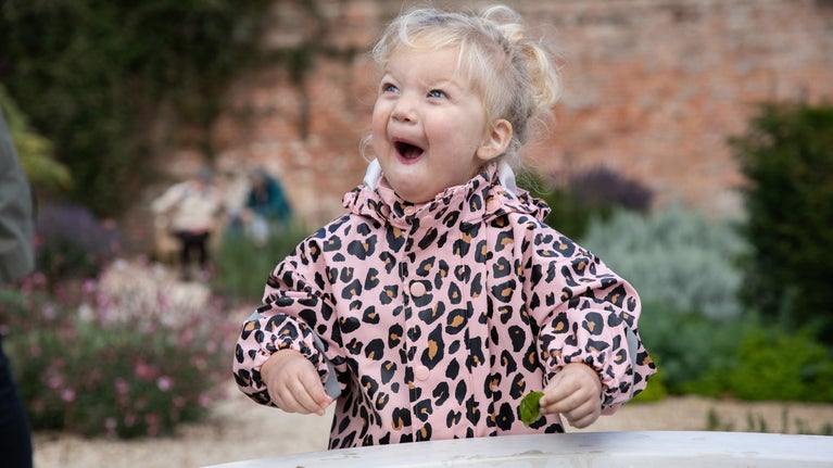 A girl looking very happy in a raincoat in a garden